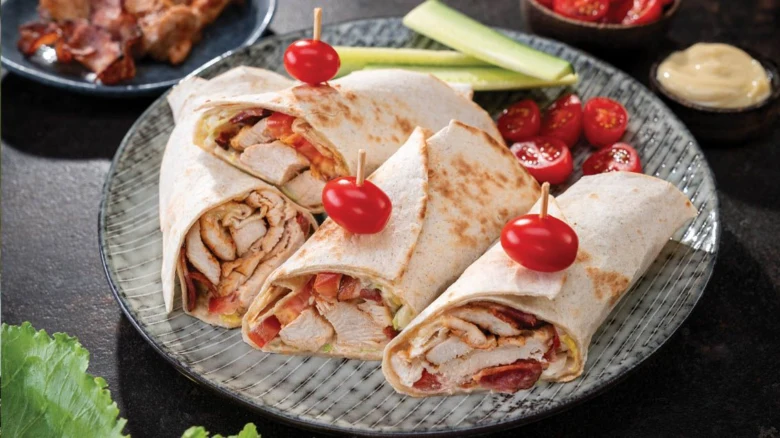 Tři nakrájené wrap s kuřetem a slaninou na talíři.