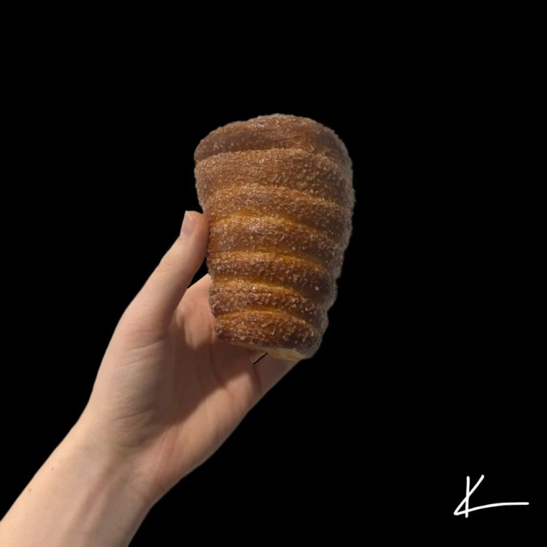 Ruka drží domácí trdelník s cukrem na černém pozadí.