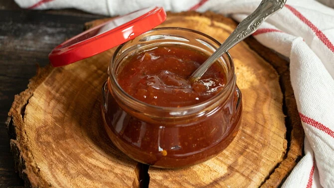 Skleněná dóza s domácí omáčkou na grilování v dřevěné podložce.