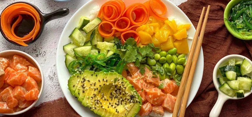 Poké s lososem, avokádem a čerstvou zeleninou na bílém talíři.