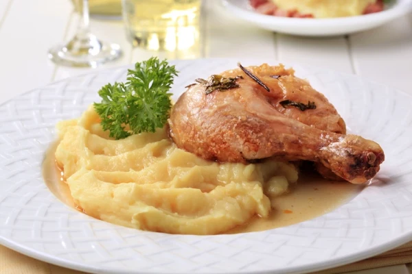 Připravená bramborová kaše s kuřecí nohou na talíři.