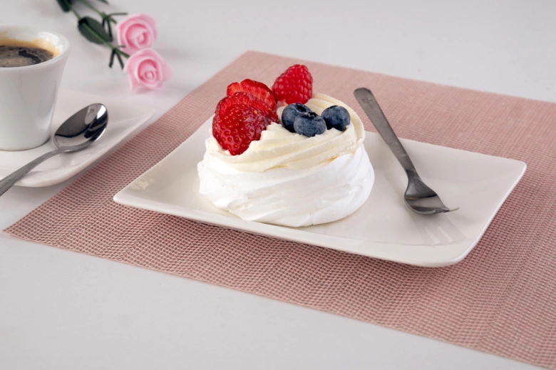 Pavlova s ovocem a smetanou na bílém talíři.
