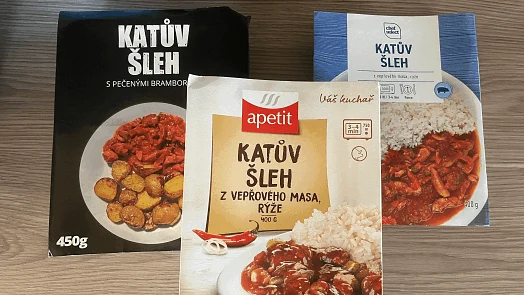 Tři balení mražených jídel s katovým šlehem na dřevěném stole.