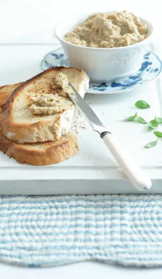 Kousek chleba s pomazánkou vedle misky plné stejného dipu.