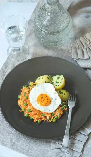 Dušená mrkev s hráškem pod smaženým vejcem na talíři.