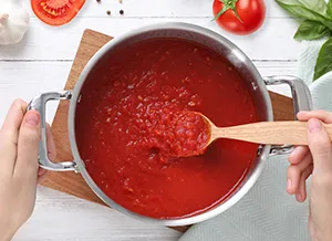 Ruční míchání domácího rajčatového sugo v hrnci s čerstvými ingrediencemi.