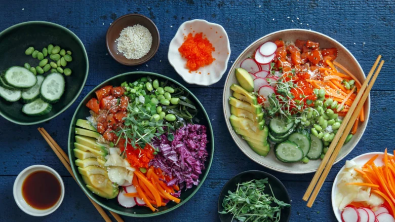 Dva poké bowl s čerstvými zeleninovými přílohami a omáčkami.