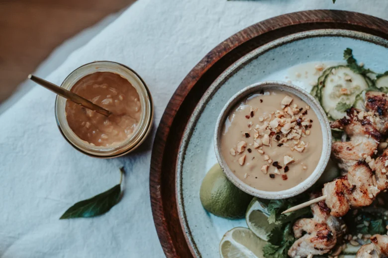 Grilované kuřecí satay s arašídovou omáčkou na dřevěném podnosu.