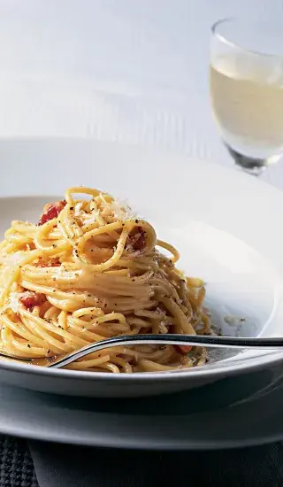 Miska se spagetti carbonara s kousky šunky a čerstvým pepřem.