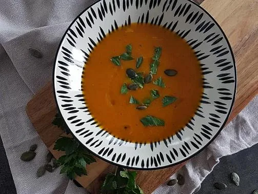 Dýňová polévka v misce s bylinkami na dřevěném podkladu.