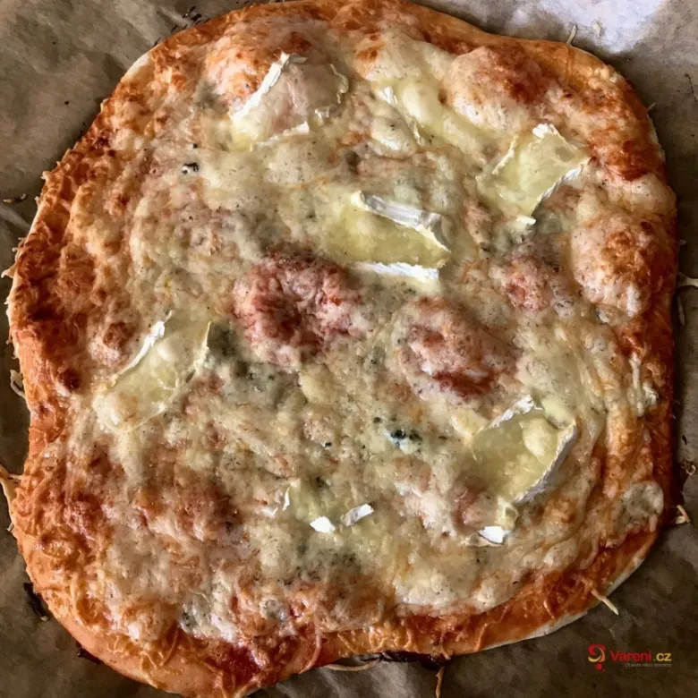 Domácí pizza s rozteklým sýrem, bylinkami na pečicím papíru.