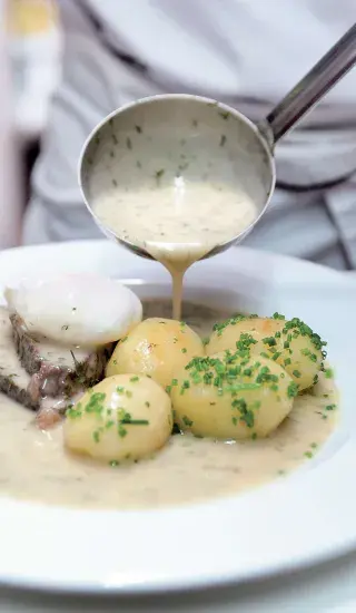 Koprová omáčka nalévána na maso s bramborami.