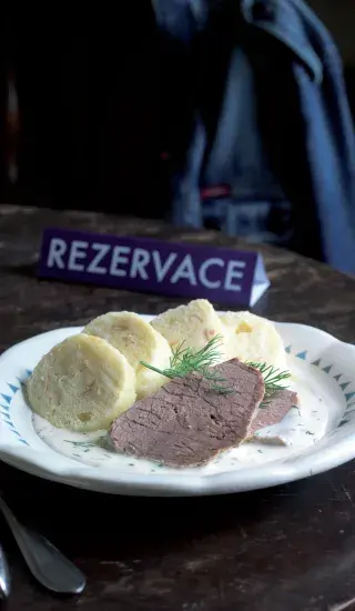 Porce hovězího masa s koprovou omáčkou a knedlíky na talíři.