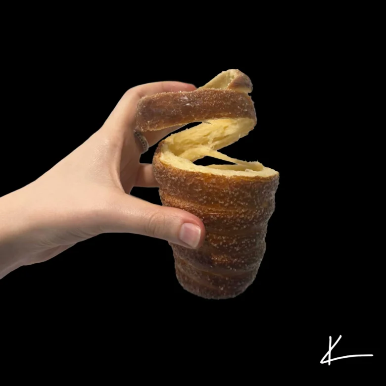 Ruce drží roztržený cukrový trdelník s viditelnou vnitřní strukturou.