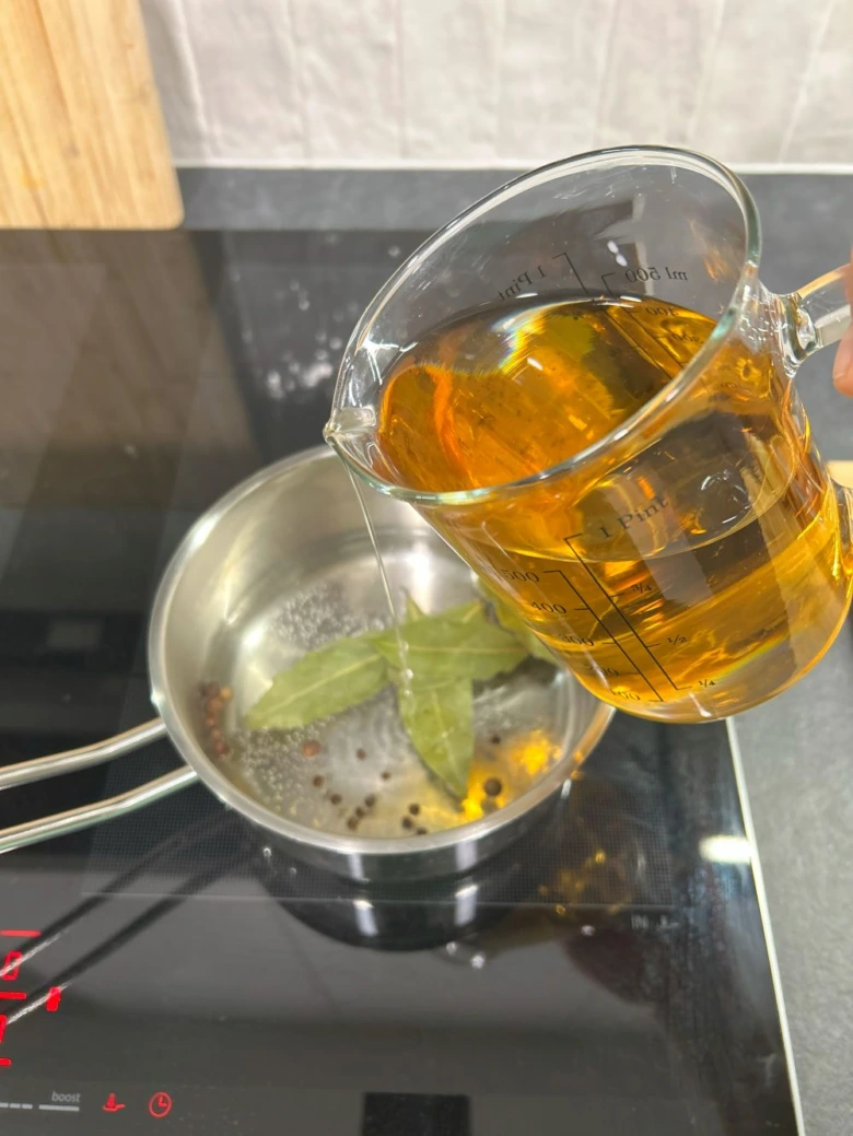 Nalévání vývaru do hrnce s listy vavřínové a pepře.