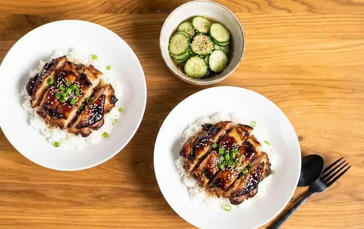 Dva talíře s kuřecím masem v omáčce teriyaki na rýži.