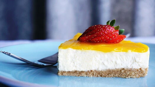 Kousek ovocného cheesecaku s jahodou na modrém talíři.