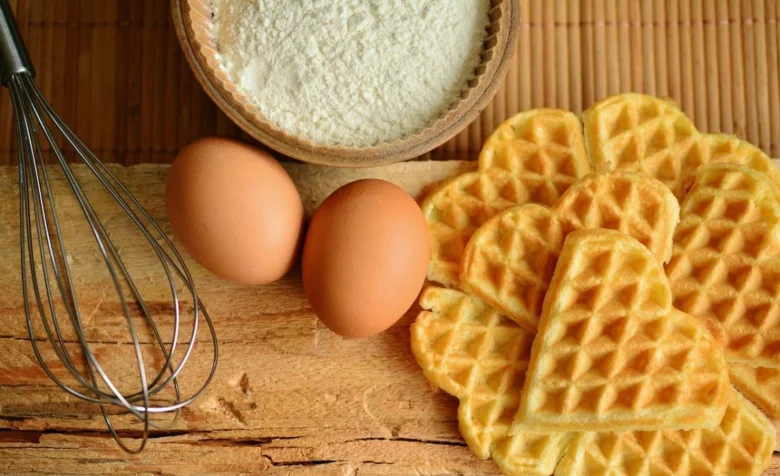 Zlaté vaflí s vejci moukou a šlehačem na dřevěném prknu.