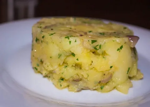 Kousek domácí bramborové krokety s cibulí na bílém talíři.