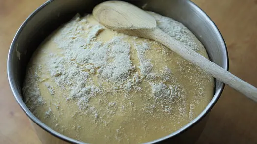 Těsto v míse posypané moukou s dřevěnou lžící.