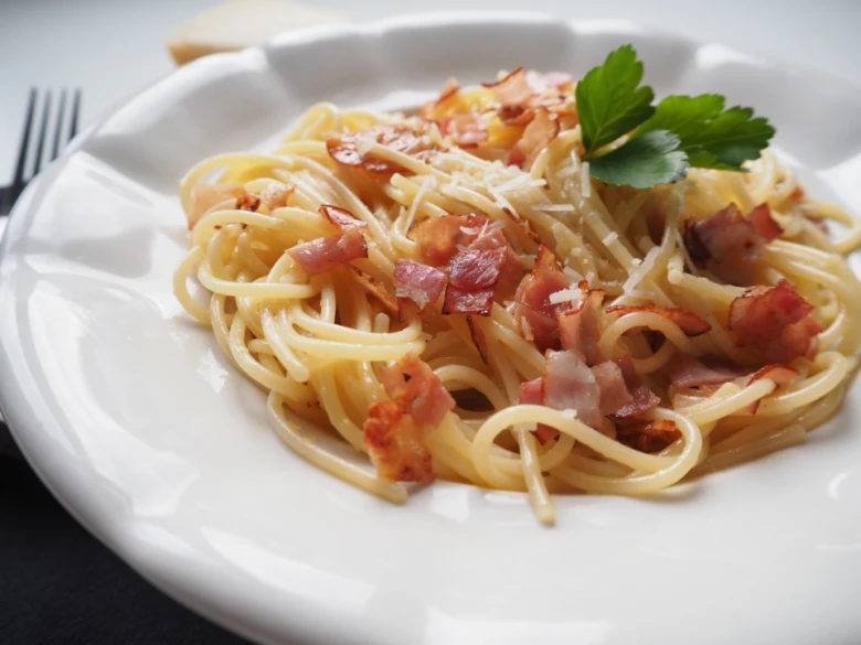 Špagety Carbonara s křupavým bůčkem na bílém talíři.