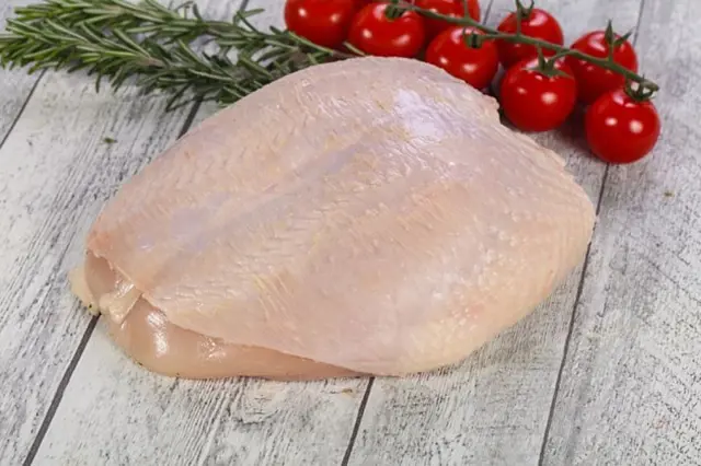 Surové kuřecí prsa s rajčaty a rozmarýnem na dřevěném povrchu.