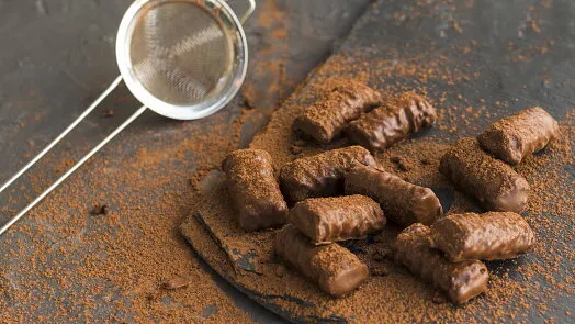 Hotové čokoládové rolády posypané kakaem vedle síta.