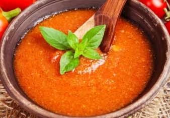 Červená polévka gazpacho s čerstvou bazalkou v hrnci.