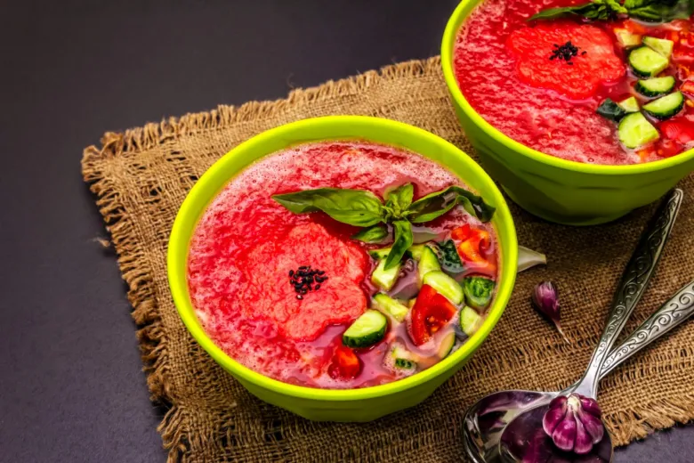 Dvě misky červené polévky gazpacho s bazalkou a okurkou.