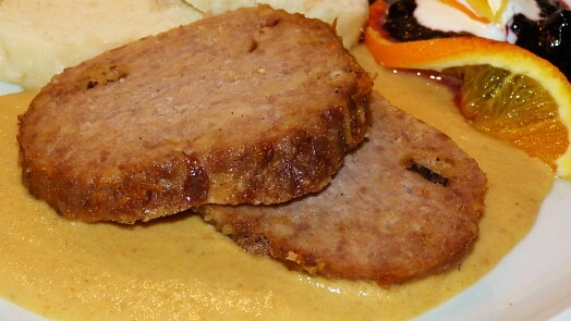 Dva plátky vepřové sekané s omáčkou, bramborami a ovocem.