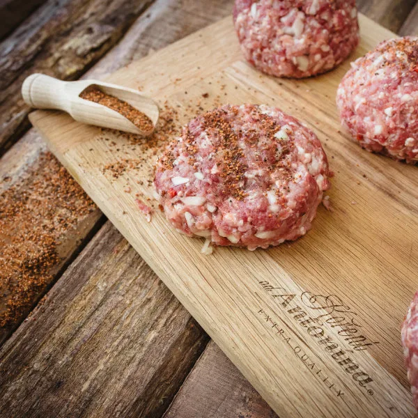 Surová masa na burgery s kořením na dřevěném prknu.