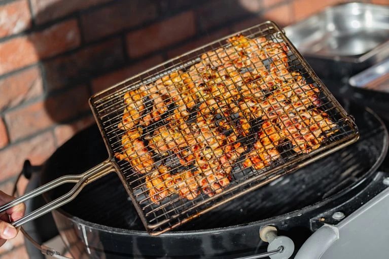 Grilovaný bůček v mřížce na otevřeném uhlíkovém grilu.