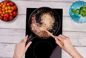Ruční míchání rýže s cibulí v pánvi na indukci pro vegetariánské rizoto.