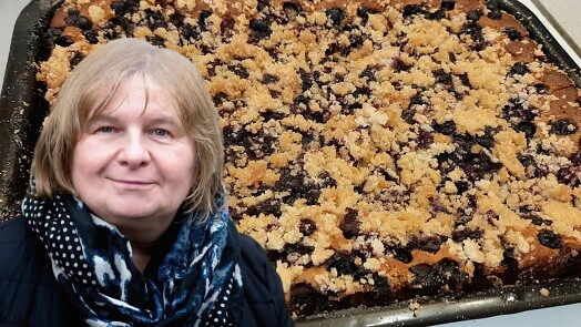Žena stojí vedle velkého plechu s koláčem z rybízu a tvarohu.