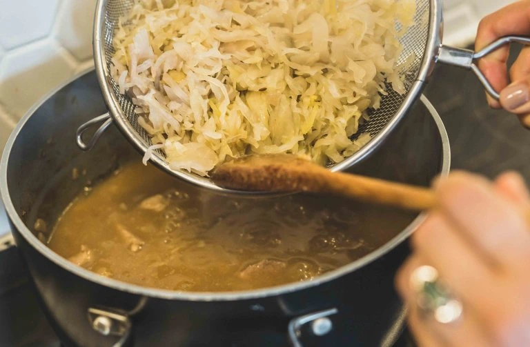 Přidávání kysané zeliny do guláše v hrnci
