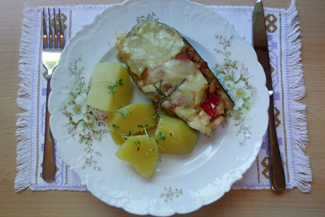 Zapečený lilek s bramborami na talíři.