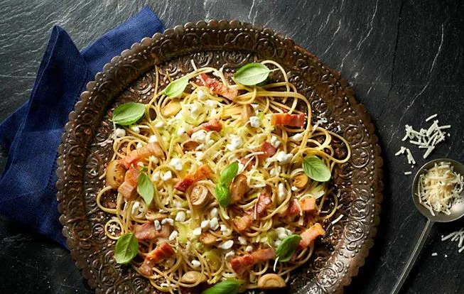 Pasta s bazalkou, slaninou a houbami na ozdobném talíři.