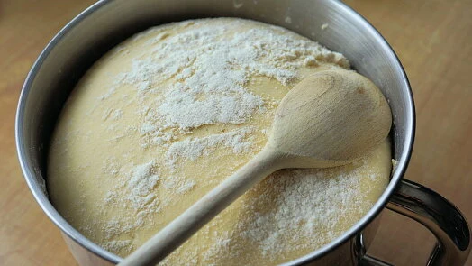 Kysnuté těsto v míse posypané moukou s dřevěnou lžící.