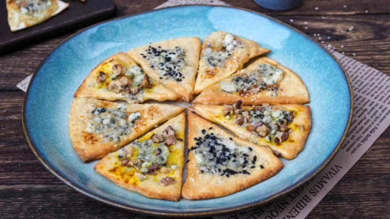 Pizzové kousky s sýrem a ořechy na modrém talíři.