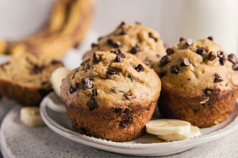 Zlatohnědé banánové muffiny s čokoládovými kousky na bílém talíři.