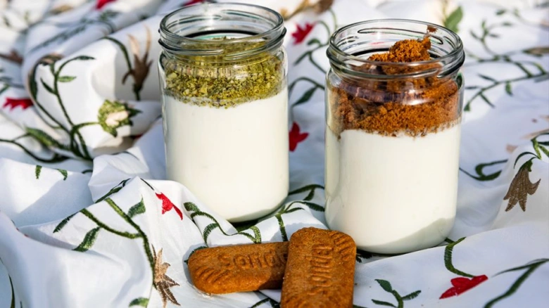 Jogurt s posypkou a sušenkami na bílém ubrusu.