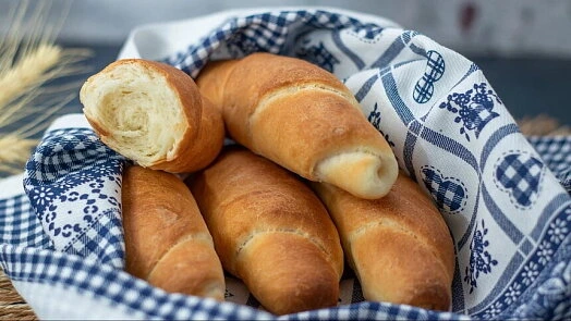 Zlatohnědé domácí rohlíky v košíku s modrobílým ubrusem.