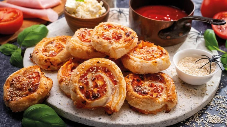 Zlatohnědé pečené pizzové šneky s rajčatovou omáčkou, sýrem a sezamem na talíři.