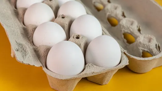 Bílé vejce v kartonovém podnosu na žlutém pozadí.