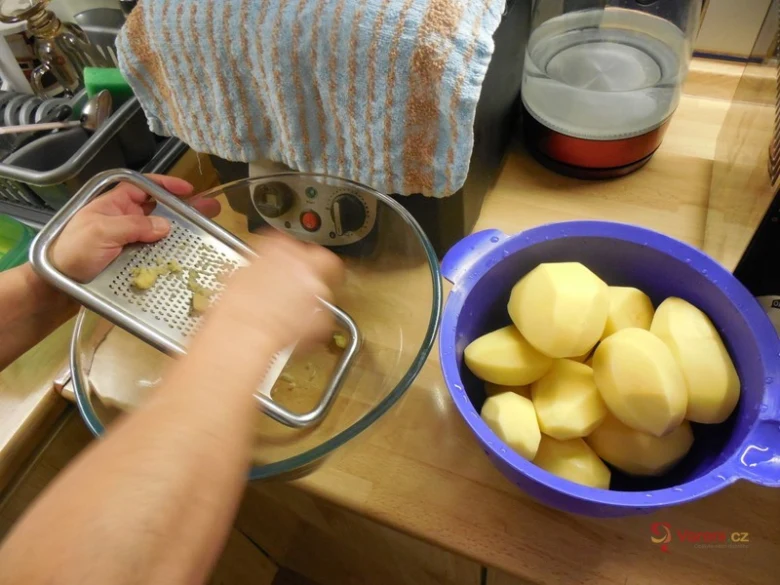 Lidé třou brambory na struhadle do skleněné misky.