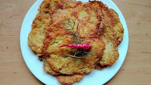 Zlaté bramborové placky na bílém talíři s paprikou.