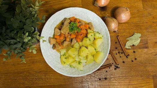 Mísa s dušeným vepřovým masem, mrkví a bramborami na dřevěném stole.