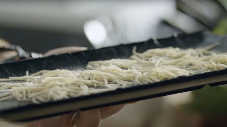 Ruce drží plech s suchými nudlemi připravenými pro recept.