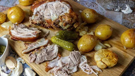 Upečené vepřové s bramborami, okurkami a cibulí na dřevěném talíři.