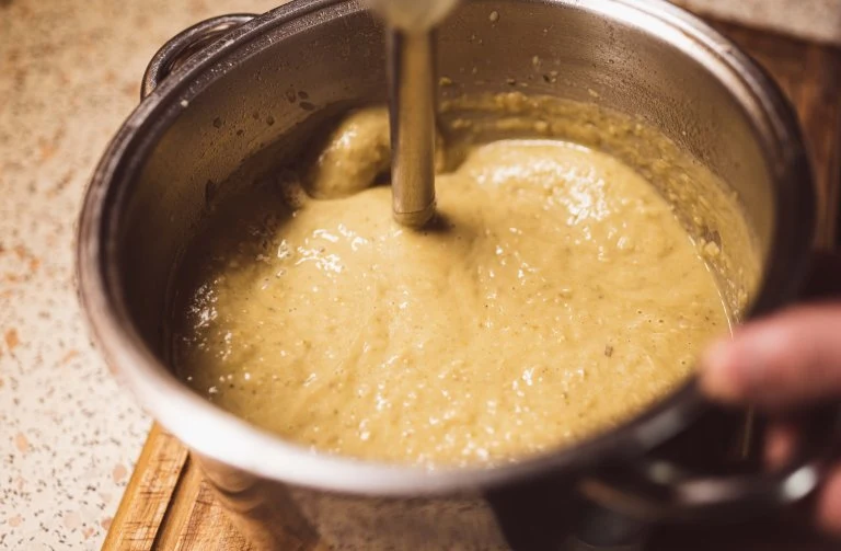 Křupavá hrachová polévka se míchá v hrnci pomocí mixéru.